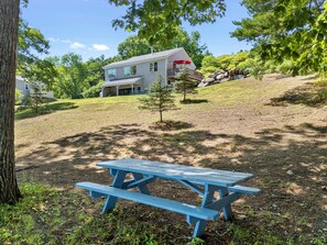 Une table de pique-nique dans un espace herbeux, avec une maison en arrière-plan.