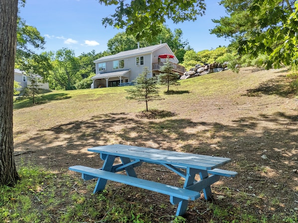 Una mesa de picnic en un área con césped, con una casa al fondo.