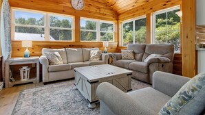 A cozy cabin interior with wooden walls, a sofa, a loveseat, a coffee table, and a clock on the wall.