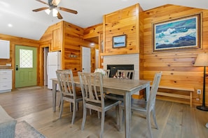 Un interior de madera con una mesa de comedor, sillas, un refrigerador, una puerta verde y una chimenea.