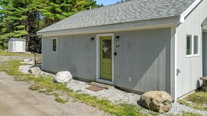 A small, single-story building with a green door, a window, and a number '67' on the wall.