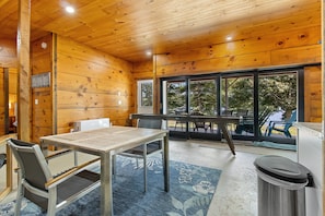 Un intérieur en bois avec une table et des chaises, une poubelle et une vue sur l’extérieur grâce à de grandes fenêtres.