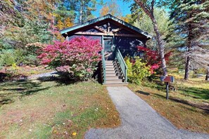 A small wooden cabin with a staircase leading to a door, surrounded by trees and shrubs. - Dog-friendly cabin retreat with kitchen, firepit, hiking & outdoor fun (Northport)