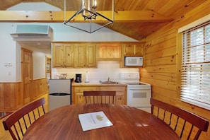 A wooden cabin interior with a dining table, chairs, a kitchen with wooden cabinets, a microwave, and a stove. - Dog-friendly cabin retreat with kitchen, firepit, hiking & outdoor fun (Northport)