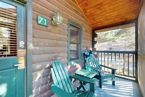 Una cabaña de madera con un porche, dos sillas Adirondack, un letrero con el número '71' y una ventana con contraventanas.
