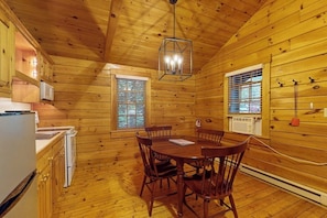 Interior de una cabaña de madera con cocina, mesa de comedor y sillas.