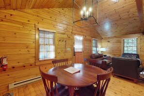 Ein Interieur einer Holzhütte mit Esstisch, Stühlen, einer Couch und einem Kamin.