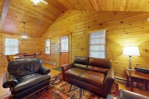 Interior de una cabaña de madera con un sofá de cuero, una mesa de comedor y una lámpara.