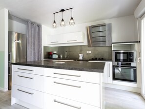 A modern kitchen with stainless steel appliances, white cabinetry, and a marble countertop. - Appartement Casau - Welkeys (Anglet)