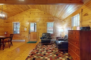 A log cabin interior with a dining table, two leather chairs, a fireplace, and a patterned rug. - Idyllic dog-friendly studio cabin with AC, fireplace & WiFi (Northport)