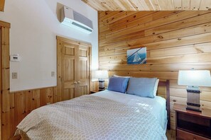 Ein Schlafzimmer mit Holzboden, einem Bett mit gemustertem Überwurf, zwei Nachttischlampen und einer Wand-Klimaanlage.