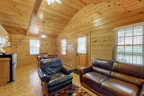 A log cabin interior with a dining area, a leather sofa, and a kitchen. - Dog-friendly nature lovers retreat with fireplace, WiFi, AC & playground (Northport)