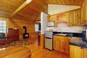 A wooden cabin interior with a kitchen, dining area, and a fireplace.