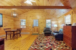 A log cabin interior with a dining table, chairs, a sofa, a TV, and a patterned rug.