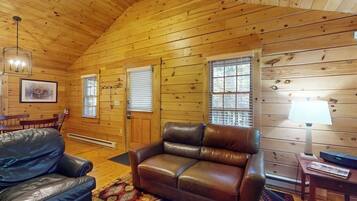 A wooden cabin interior with a leather sofa, a dining table, and a lamp.