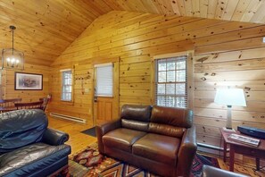 A wooden cabin interior with a leather sofa, a dining table, and a lamp. - Escape to a dog-friendly cabin w/streaming, kitchen, fireplace & nature nearby (Northport)