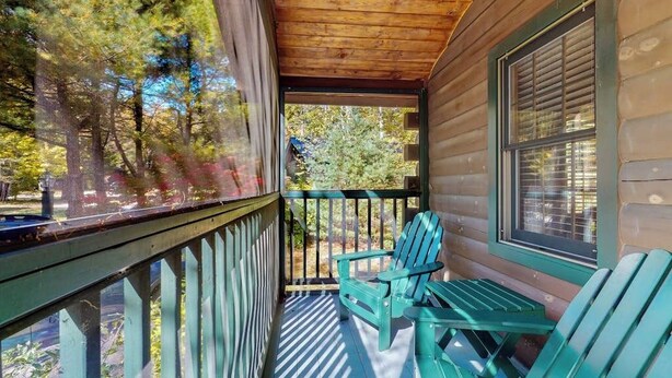 Een veranda met houten leuningen en twee groene Adirondack-stoelen.