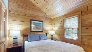 Een kamer met houten lambrisering, een bed, twee bedlampjes, een lijst met een afbeelding en een raam.