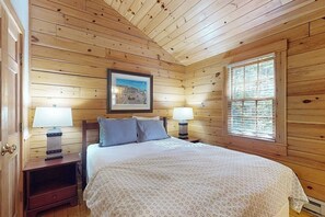 A wooden-paneled room with a bed, two bedside lamps, a framed picture on the wall, and a window. - Escape to a dog-friendly cabin w/streaming, kitchen, fireplace & nature nearby (Northport)