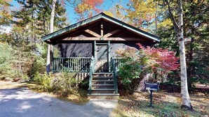 Een houten chalet met een veranda en een trap die erheen leidt, omringd door bomen en een brievenbus.