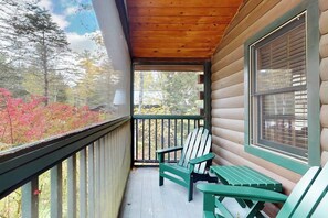 A wooden porch with Adirondack chairs, a window, and a view of trees and foliage. - Serene two-bedroom dog-friendly cabin getaway with kitchen, fireplace & more (Northport)