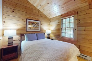 Ein Schlafzimmer mit Holzwand, einem Bett, zwei Nachttischen mit Lampen, einem gerahmten Bild an der Wand und einem Fenster.