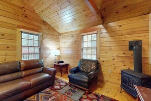 Ein Holzblockhaus-Interieur mit Sofa, Sesseln, Teppich und Kaminofen.
