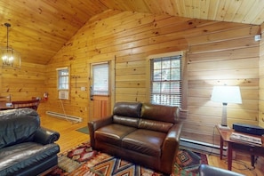 Ein Holzblockhaus-Interieur mit Ledersofa, Esstisch und Lampe.