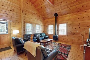 Ein Holzblockhaus-Interieur mit Kamin, Ledersofas, einem Couchtisch und einem gemusterten Teppich.