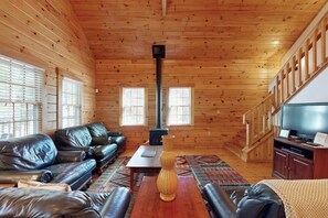 Ein Blockhaus-Interieur mit einer Couch, einem Couchtisch, einer Vase, einem Kamin und einem Fernseher.