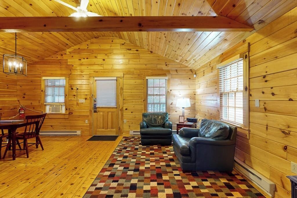 L’intérieur d’une cabane en rondins, avec une table à manger, des chaises, un canapé, un tapis à motifs et un ventilateur de plafond.