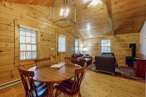 A wooden cabin interior with a dining table, chairs, a sofa, and a fireplace.