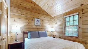 Camera da letto in legno con un letto, due comodini, una finestra e un quadro appeso al muro.