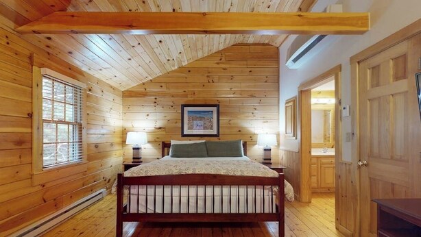 Ein Schlafzimmer mit Holzwänden, einem Bett, Nachttischlampen und einem gerahmten Bild an der Wand.