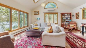 A spacious living room with large windows, a fireplace, a bookshelf, and a comfortable seating area.