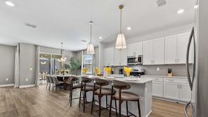 A modern kitchen with white cabinets, stainless steel appliances, and bar stools. - Brand New | 6BR Reunion Pool & Spa Villa 7894 (Kissimmee)