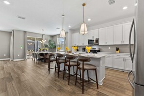 A modern kitchen with white cabinets, stainless steel appliances, and bar stools. - Brand New | 6BR Reunion Pool & Spa Villa 7894 (Kissimmee)