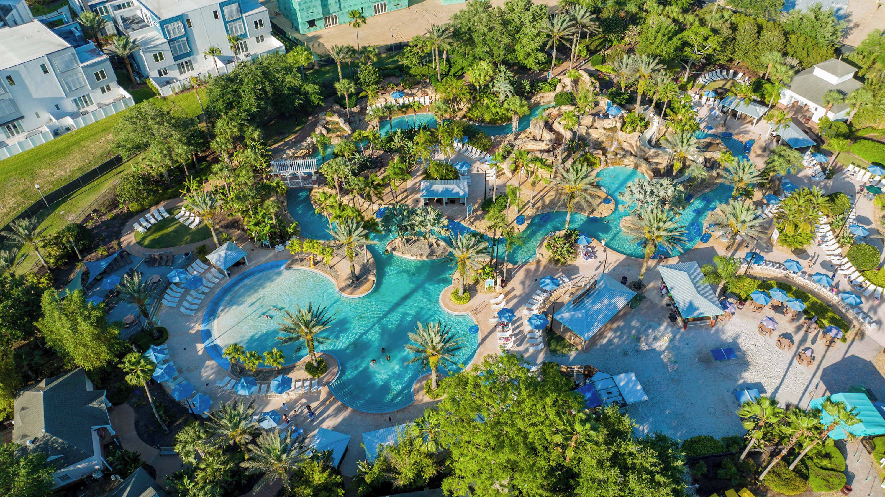 Ein Luftbild eines Resorts mit mehreren Schwimmbecken, Liegestühlen und Palmen.