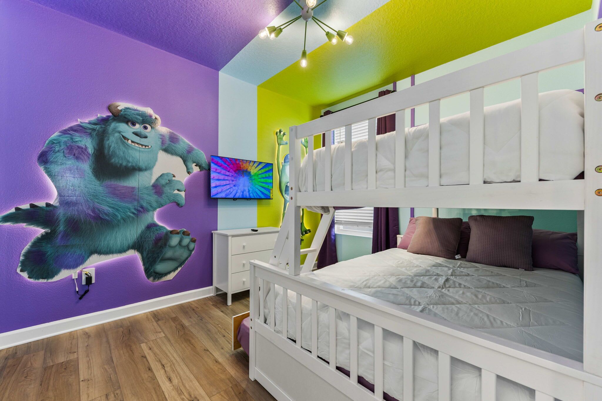 Une chambre d’enfant avec un lit superposé, une fresque murale, une télévision et un plancher en bois.