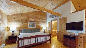 Quarto com painéis de madeira, cama, abajures, televisão e um armário de madeira.