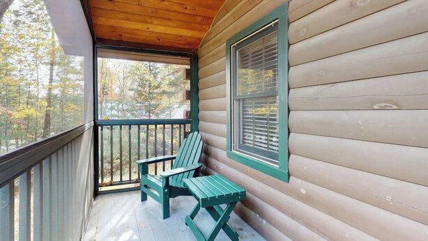 Uma cabana de madeira com varanda, uma cadeira Adirondack verde e uma janela com persianas.