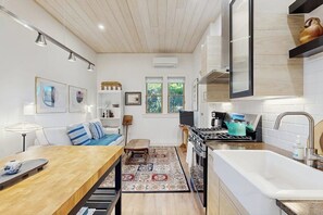A modern kitchen with a wooden countertop, a stove, and a sink. There is a dining area with a table and chairs, and a sofa.