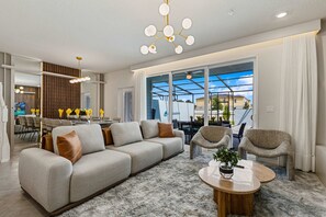 A modern living room with a sofa, chairs, a coffee table, and a dining area with a table and chairs. - Brand New | 5BR Pool, Slide & Game Loft 16172 (Clermont)