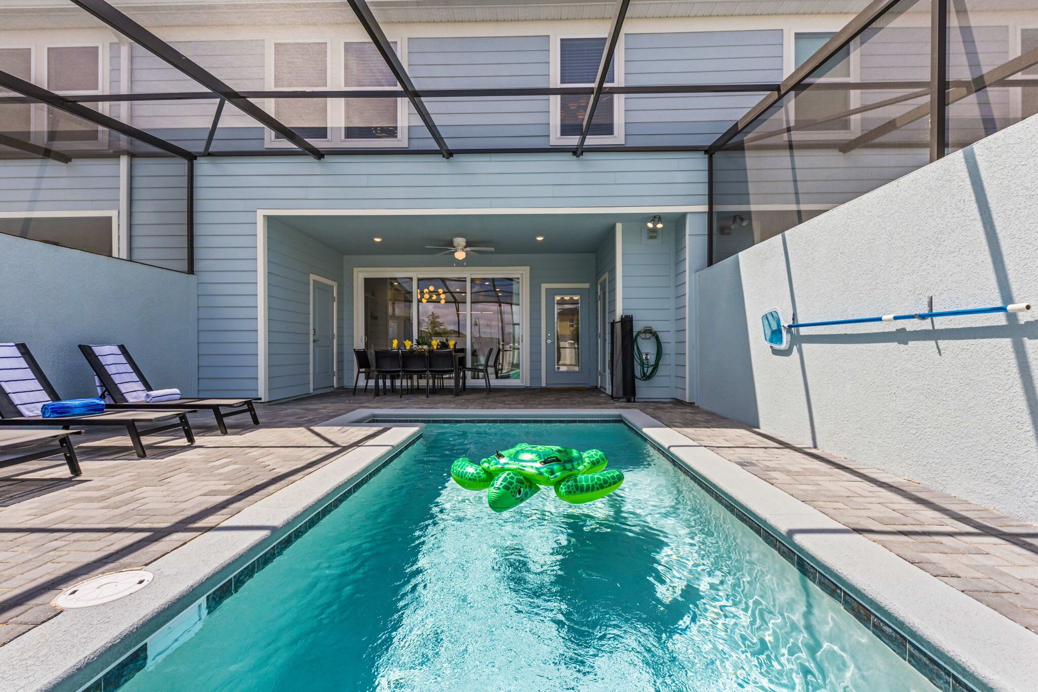 A swimming pool with inflatable toys, a covered patio area, and a dining table setup.