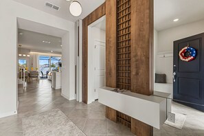 A modern interior with a wooden accent wall, a glass console table, and a dark door with a wreath. - Brand New | 5BR Pool, Slide & Game Loft 16172 (Clermont)