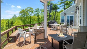 A covered outdoor deck with wooden flooring, white chairs, a table, and a grill. - Elegant ocean view home with breathtaking views, private hot tub & large deck (Rockport)