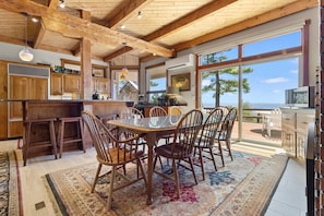 A spacious kitchen with wooden cabinets, a dining table with chairs, and a large window overlooking the sea.