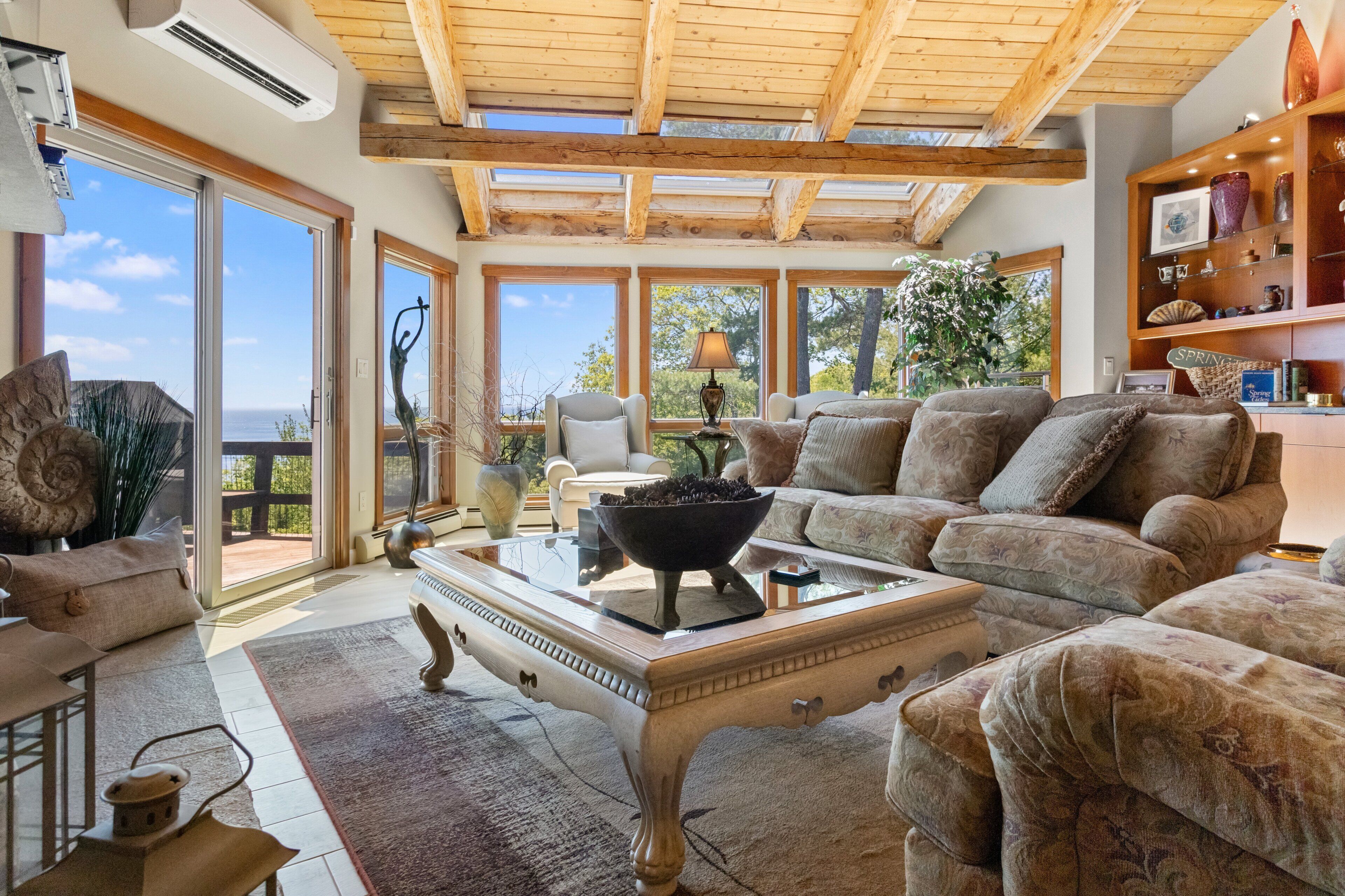Un salon spacieux avec un grand canapé, une table basse et une cheminée. De grandes fenêtres offrent une vue sur l’extérieur.