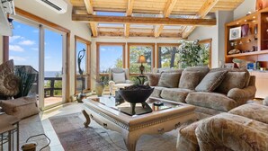A spacious living room with a large sofa, a coffee table, and a fireplace. There are large windows providing a view of the outdoors. - Elegant ocean view home with breathtaking views, private hot tub & large deck (Rockport)