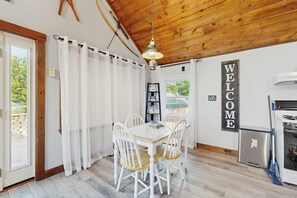 A dining area with a white table and chairs, a wooden ceiling, and a 'WELCOME' sign. - Scenic retreat with a spacious deck, gas fireplace, and Moosehead Lake views (Greenville)